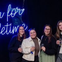 Group of 5 girls together in front of neon sign